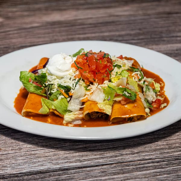 Three enchiladas covered in red sauce, topped with lettuce, pico de gallo, cheese, and sour cream.