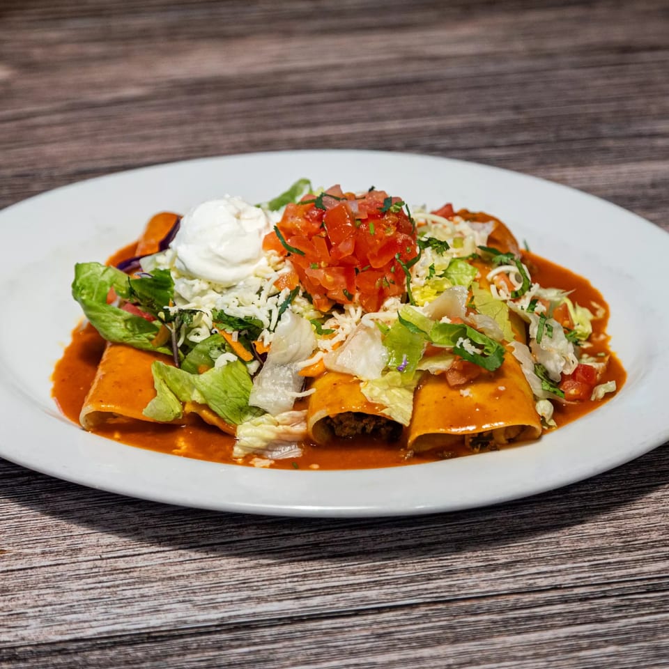 Three enchiladas covered in red sauce, topped with lettuce, pico de gallo, cheese, and sour cream.