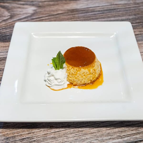 Flan dessert with caramel sauce, whipped cream, and a mint garnish on a white plate.