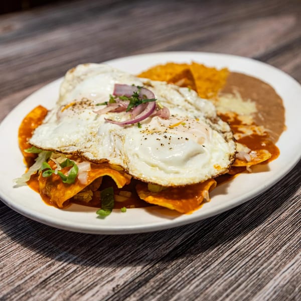 Chilaquiles with two fried eggs, red sauce, beans, and rice on a white plate.