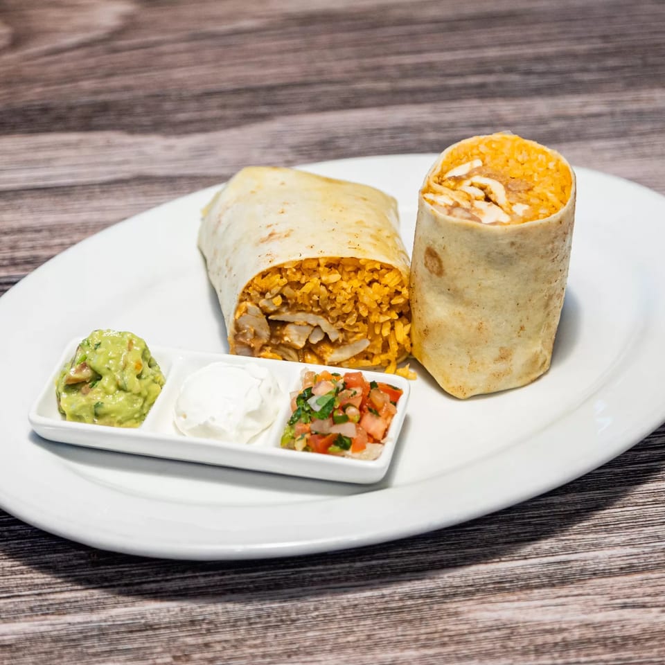 Two burritos with rice and chicken, served with guacamole, sour cream, and pico de gallo.