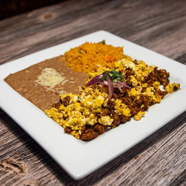 A Mexican breakfast plate with scrambled eggs and chorizo, refried beans, and Mexican rice.